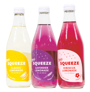 three bottles of Beas Squeeze bottled lemonade : classic(yellow), lavendar(purple), and hibiscus(pink)